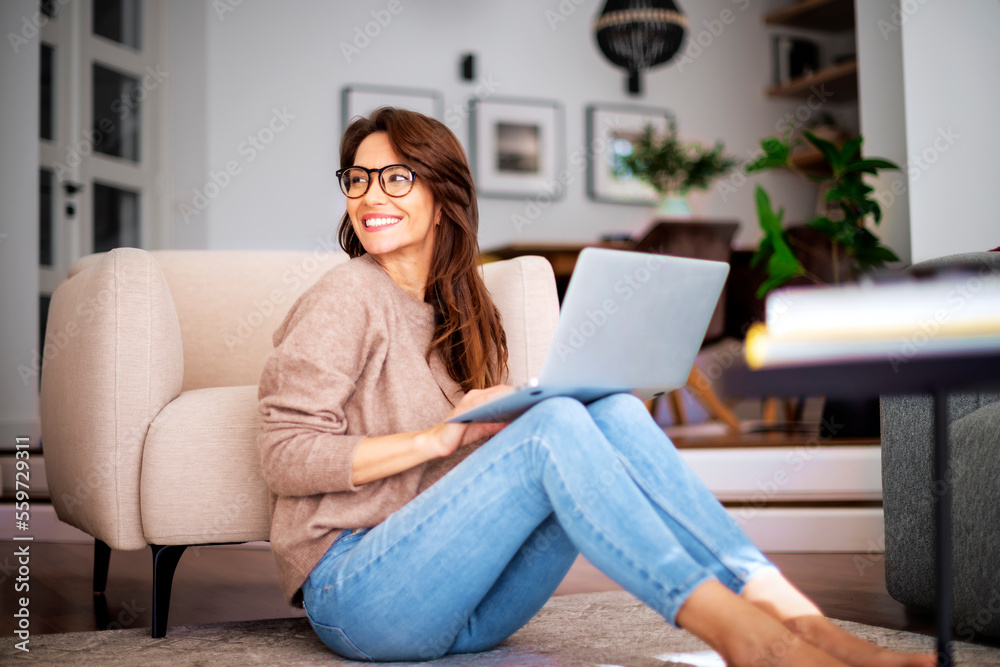 Smiling caucasian woman using laptop at home while sitting on the floor Smiling caucasian woman using laptop at home while sitting on the floor
