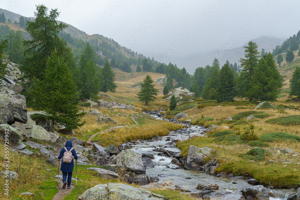 A hiker enjoys the scenic beauty of De Vallée de la Clarée in Hautes-Alpes, France, on a rainy day. The valley is known for its alpine landscapes, waterfalls and mountain lakes.
