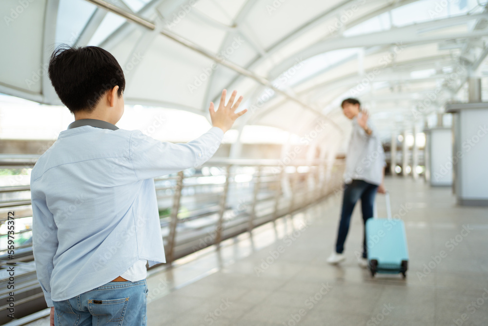 Asian little boy waves a hand and says goodbye to his father at the airport or railway terminal before father leaving. Asian little boy waves a hand and says goodbye to his father at the airport or railway terminal before father leaving.