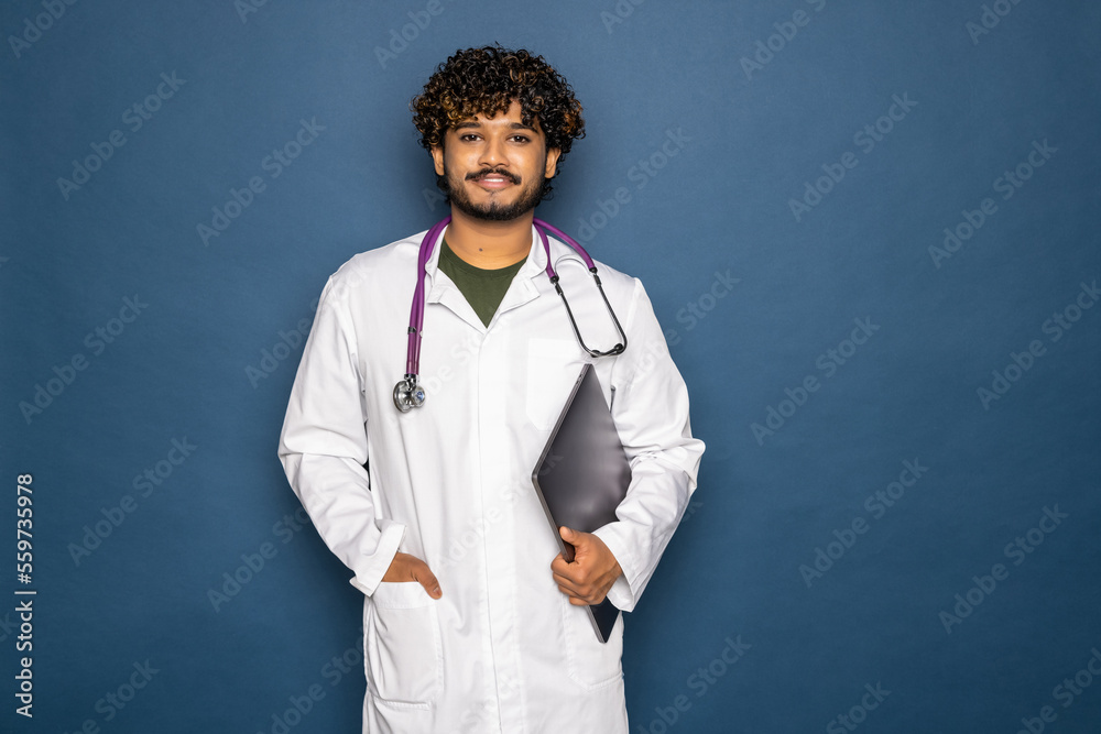 Indian doctor working with laptop, isolated on blue background Indian doctor working with laptop, isolated on blue background