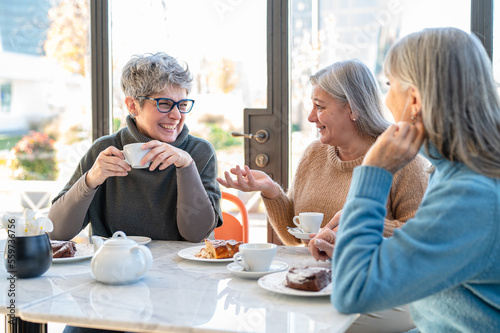 Group of elderly women having fun during breakfast in a cafeteria, three retired female friends are celebrating an anniversary, mature women drinking tea and coffee and eating cakes photo