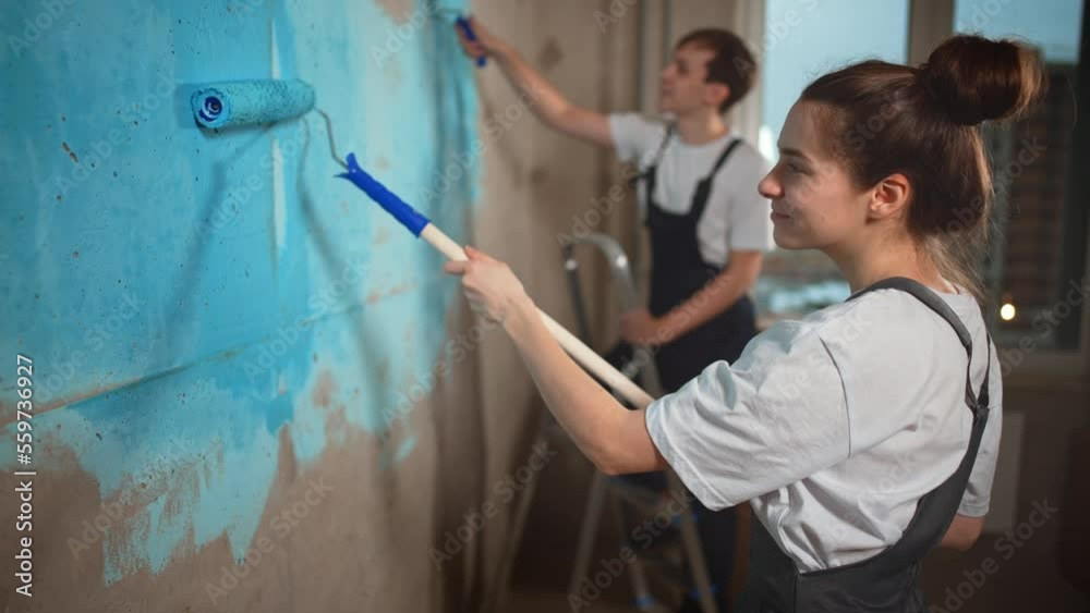 Painters, guy and girl paint walls in room with roller. Wall