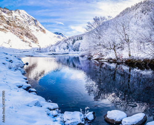 Picturesque landscape of a snowy winter mountain lake. Small lake next to the Saut Deth Pish waterfall during autumn and a snowy day, located in the Aran Valley, Pyrenees, Catalonia, Spain. photo