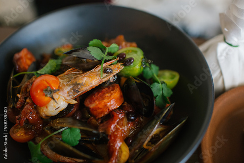 Close up shot of a bowl of large prawns with mussels topped with green leaves and tomatoes photo