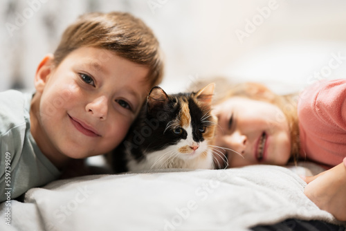 Brother and sister with kitty cat lying on the sofa. Children's love for pets.