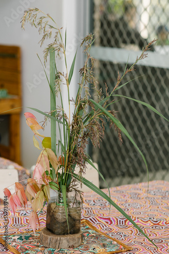 Common reed grass and lilly pilly leaves in a small container with water and rocks photo