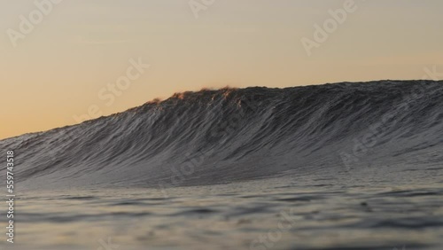 A short heavy wave crash over the shallow rock ledge as the sun rises in the background. The water is backlit in the early morning light. The sound of the waves crashing is almost deafening. photo