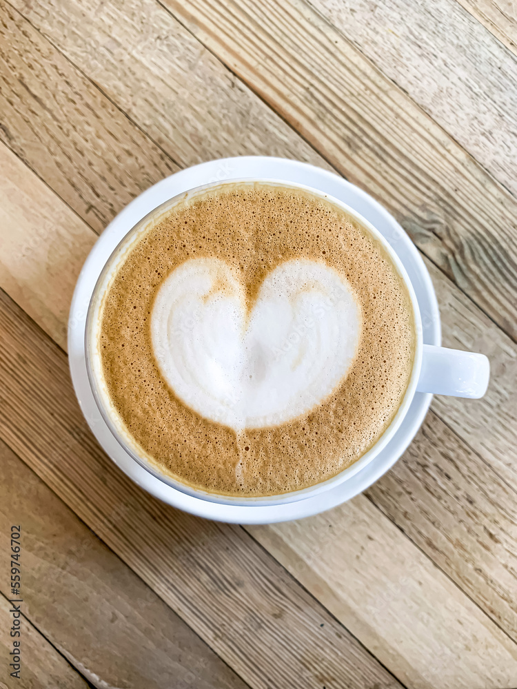 A cup of coffee latte on a wooden table. A mug of flat white coffee, latte, cappuccino on a wooden background. Coffee art. Heart flower shape latte art