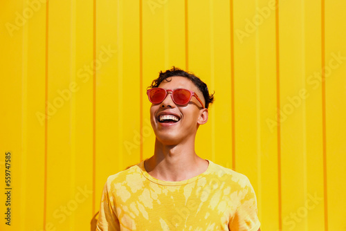 Happy young man wearing red sunglasses in front of yellow wall photo