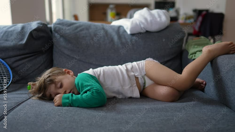 Funny little boy laying on sofa sleeping during afternoon nap. Baby toddler wearing diapers asleep on couch