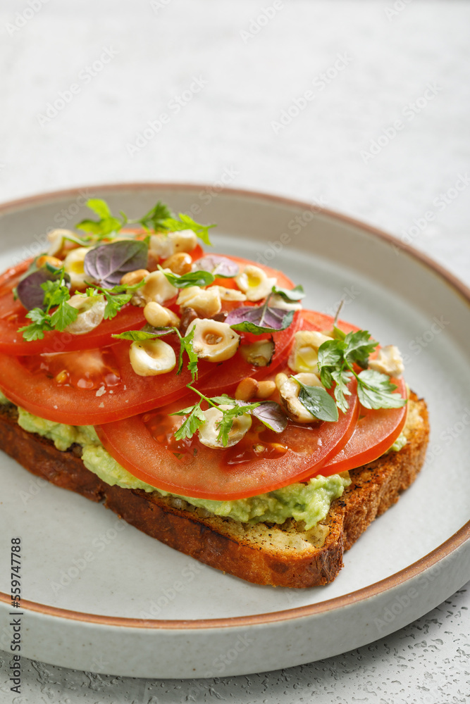 Toast with guacamole and slices of fresh tomatoes with fried hazelnuts on top. Vegetarian cuisine Toast with guacamole and slices of fresh tomatoes with fried hazelnuts on top. Vegetarian cuisine