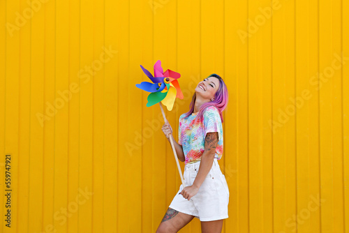 Smiling woman holding multi colored pinwheel toy in front of yellow wall photo