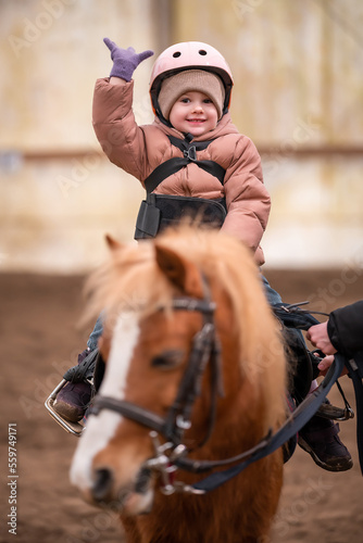 Little Child Riding Lesson. Three-year-old girl rides a pony and does exercises © dtatiana