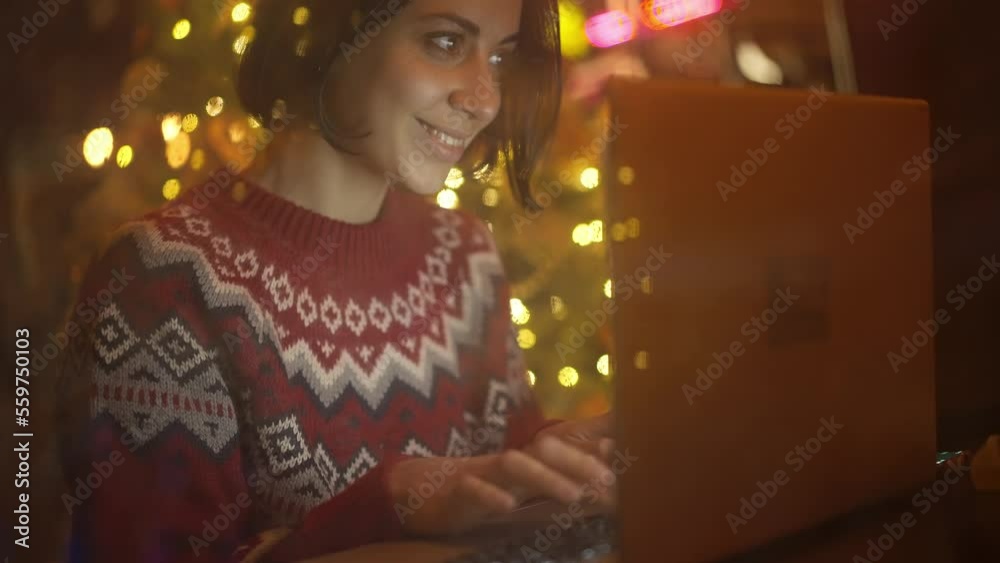 festive weared woman sits in decorated cafe close to window on Christmas Eve using laptop. girl dreamily looking at window. festive mood, making wishes, dreams concept