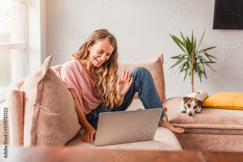 Young smiling woman waving her hand to laptop