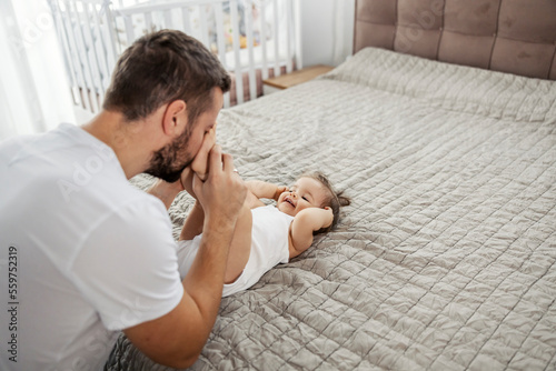 Cuadro en lienzo A little girl is lying down in bed in bedroom and laughing while her father is playing with her feet