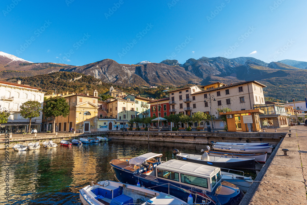 Small port of Malcesine village with small boats moored. Famous tourist resort on the coast of Lake Garda (Lago di Garda). Verona province, Veneto, Italy, Europe. Mountain range of Monte Baldo.