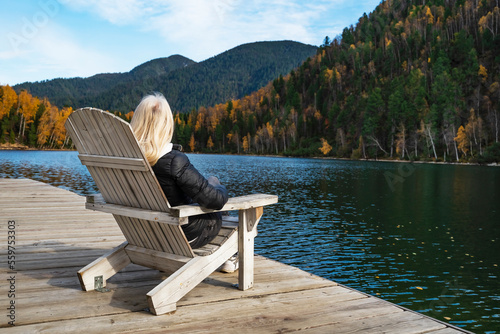 Woman resting in Comfortable wooden sun lounger Adirondack, Westport against of colorful mountains with emerald lake