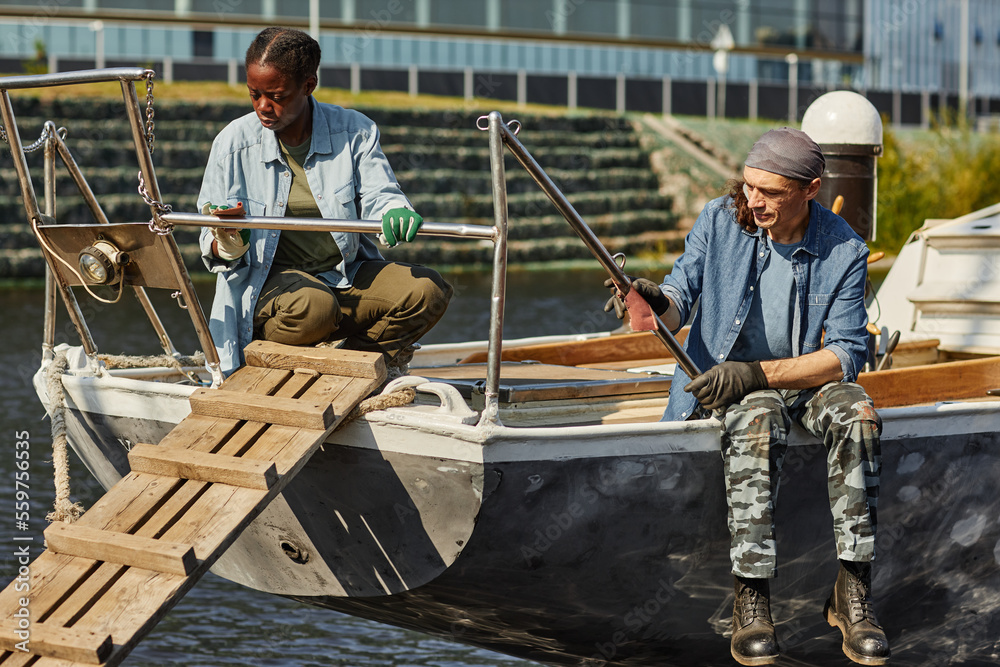 Full length portrait of man and woman on fishing boat in dock lit by sunlight, copy space Full length portrait of man and woman on fishing boat in dock lit by sunlight, copy space