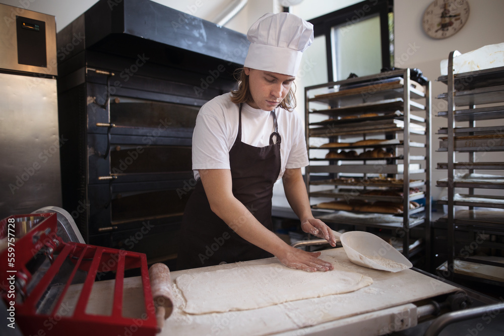 Young baker with chef cap preparing pastries in bakery. Young baker with chef cap preparing pastries in bakery.