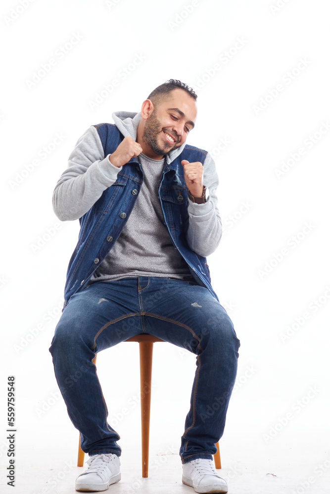 a portrait of an attractive young man in jeans shirt sitting on the chair isolated on white background, happy smiling man sitting on chair.happy emotions. a portrait of an attractive young man in jeans shirt sitting on the chair isolated on white background, happy smiling man sitting on chair.happy emotions.