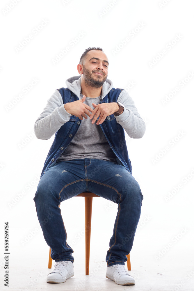 a portrait of an attractive young man in jeans shirt sitting on the chair isolated on white background, happy smiling man sitting on chair.happy emotions. a portrait of an attractive young man in jeans shirt sitting on the chair isolated on white background, happy smiling man sitting on chair.happy emotions.
