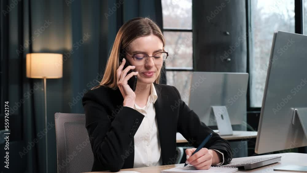 Focused businesswoman working on laptop computer in office interior. Female worker making phone call. Woman talking on smartphone at remote workplace. Business woman calling phone at modern office. Focused businesswoman working on laptop computer in office interior. Female worker making phone call. Woman talking on smartphone at remote workplace. Business woman calling phone at modern office.