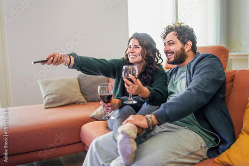Fototapeta Loving couple drinking wine and watching tv sitting on the couch