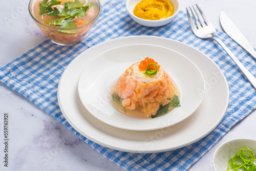 Portioned fish aspic of shrimp, salmon and boiled quail eggs decorated with red caviar and green onions on a white plate on a light background. Recipes fish and seafood. photo