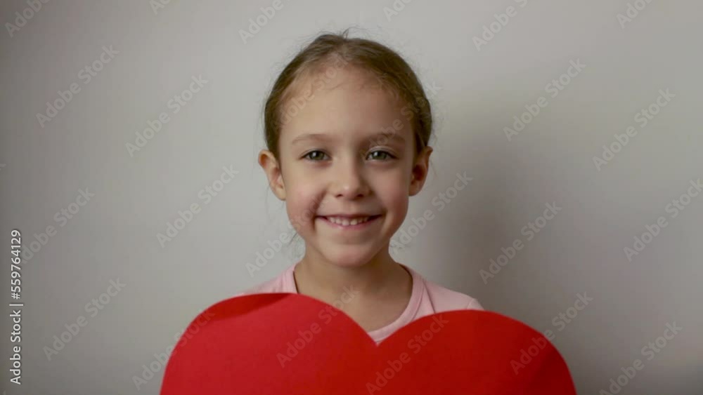 A happy girl is happy to play with a heart-shaped postcard. Valentine's Day. Celebrate. Isolated white background A happy girl is happy to play with a heart-shaped postcard. Valentine's Day. Celebrate. Isolated white background