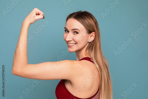 Young woman shows off her biceps on a blue background