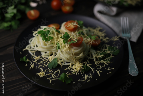 delicious fragrant pasta with grated cheese, red tomatoes, kenza greens and garlic on black plates and a wooden surface. for signboards splash screens labels banners menu flyers announcements photo