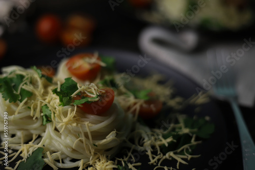 delicious fragrant pasta with grated cheese, red tomatoes, kenza greens and garlic on black plates and a wooden surface. for signboards splash screens labels banners menu flyers announcements photo