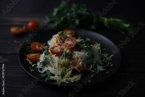 delicious fragrant pasta with grated cheese, red tomatoes, kenza greens and garlic on black plates and a wooden surface. for signboards splash screens labels banners menu flyers announcements photo