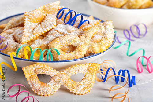 Angel wings or sfrappole or chiacchiere in shape of carnival mask. Traditional sweet crisp pastry, deep-fried, with powdered sugar. Carnival food tradition. Decorated with paper serpentine. photo