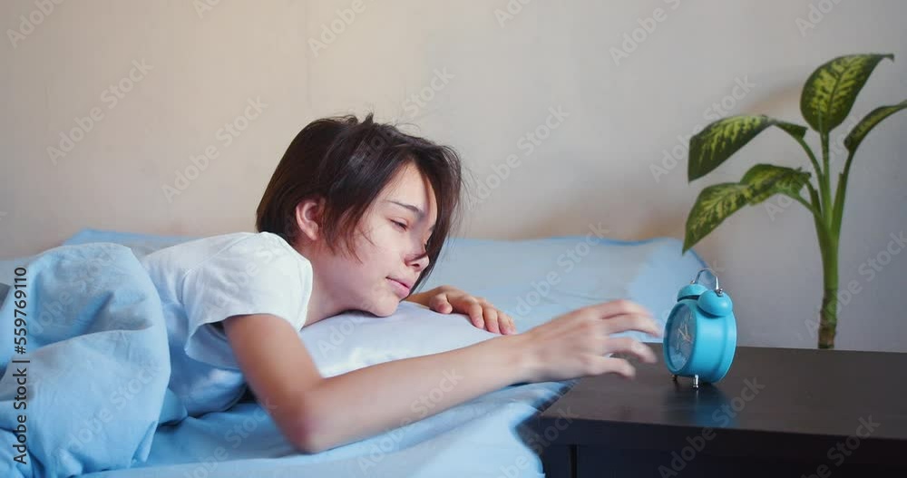 Girl sleeps, wakes up, looks at the alarm clock and falls back to sleep.