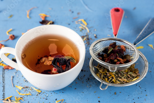 Cup of Hot and Healthy Herbal Tea with Dried Berry and Camomile Flowers Two Strainer with Herbal Tea on Blue Background