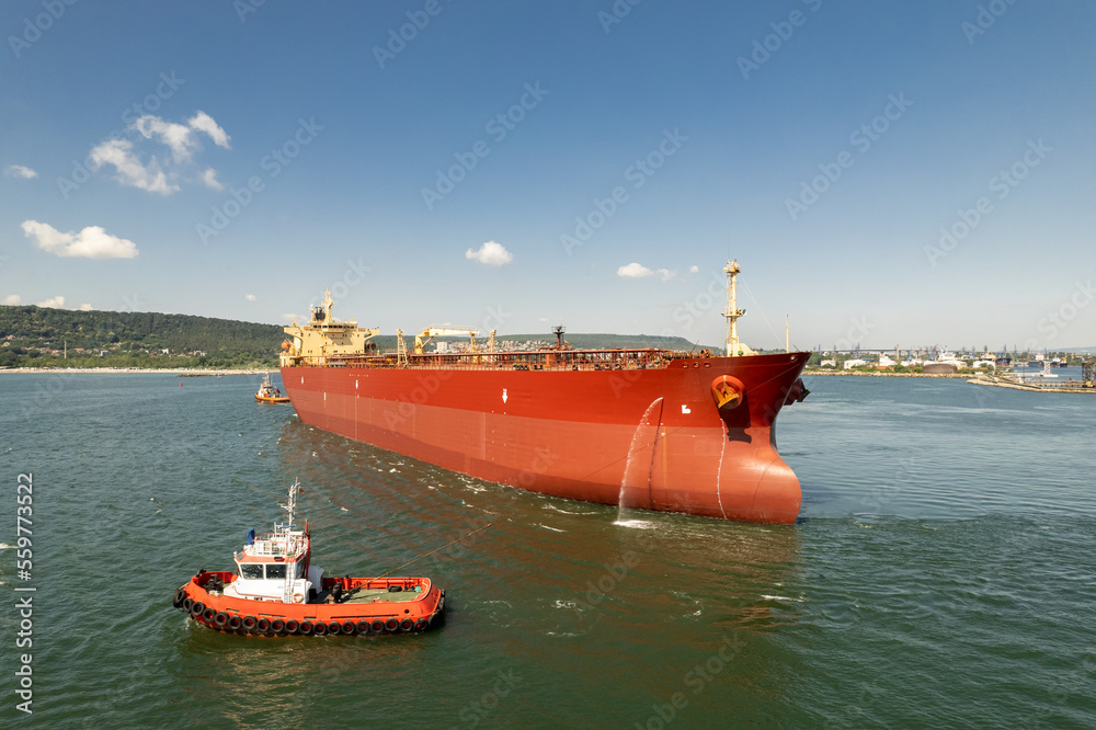 Aerial view of tug boat assisting big oil tanker. Large oil tanker ship enters the port escorted by tugboats. Aerial view of tug boat assisting big oil tanker. Large oil tanker ship enters the port escorted by tugboats.