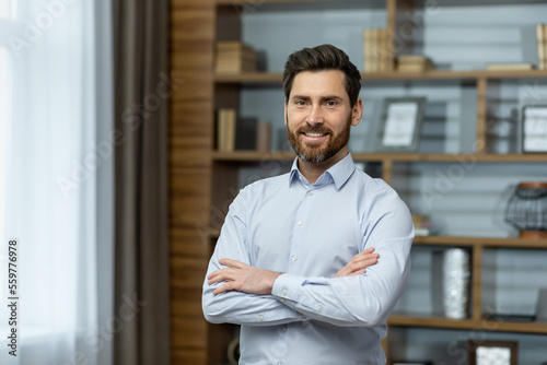 Fotografia Portrait of successful businessman in office, man in shirt smiling and looking at camera, mature boss with beard with shaggy hands standing at workplace inside building