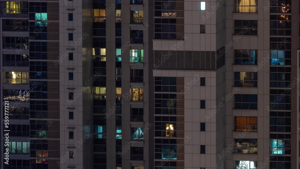 Apartment windows of a glazed skyscraper glow at night with city lights reflection aerial timelapse. Illuminated towers in business district