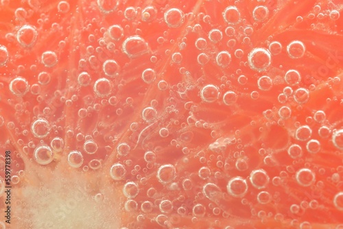 Close-up view of the red grapefruit slice in water background. Texture of cooling fruit drink with macro bubbles on the glass wall. Flat design