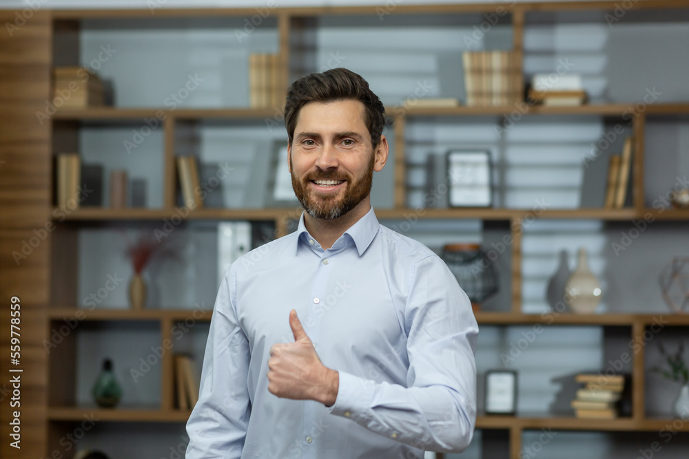 Successful businessman smiling and looking at camera, man shows thumbs up affirmatively and joyfully agrees with achievement, boss in shirt inside office at work. Successful businessman smiling and looking at camera, man shows thumbs up affirmatively and joyfully agrees with achievement, boss in shirt inside office at work.