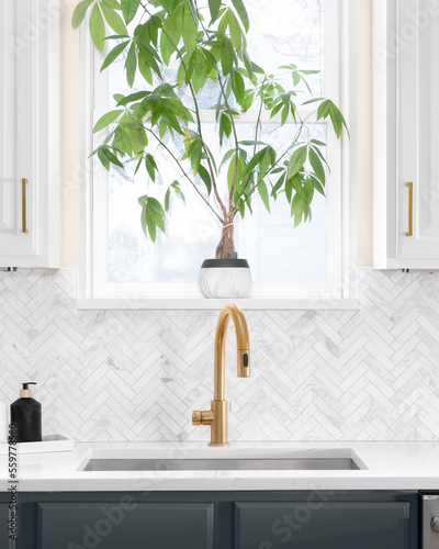 Sink detail shot in a luxury kitchen with herringbone backsplash tiles. white marble countertop  and gold faucet. 