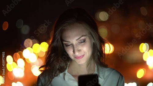 Closeup portrait of beautiful woman using smart phone on night cityscape background with street lights chatting or video talk