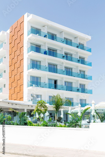 A modern building of a small hotel with a swimming pool against a blue clear sky. Vertical.
