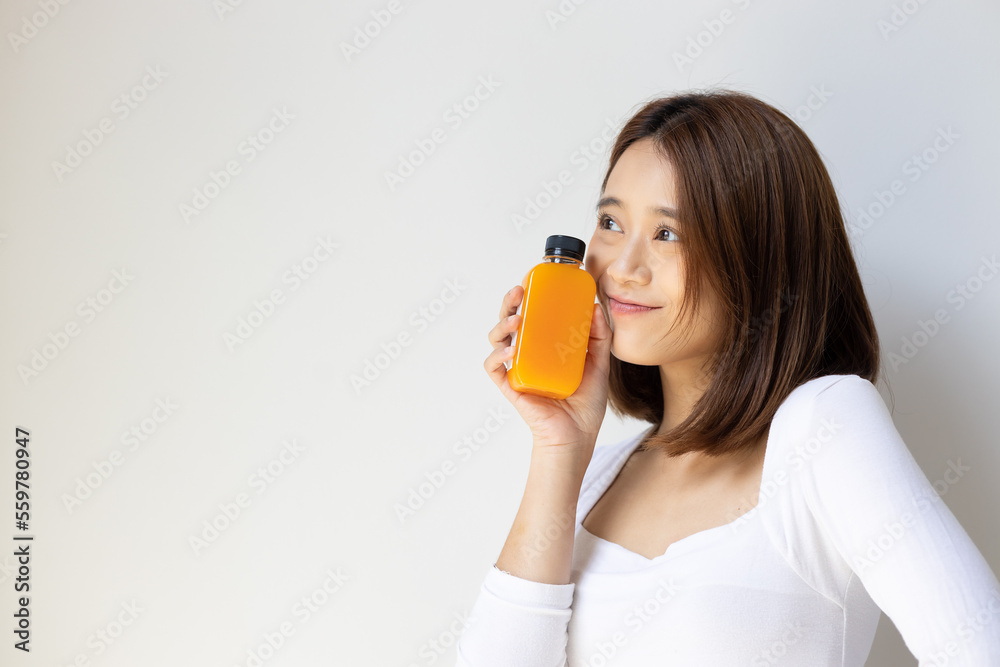 Happy and healthy asian young woman looking up and holding a bottle of fresh and raw cold pressed orange juice Happy and healthy asian young woman looking up and holding a bottle of fresh and raw cold pressed orange juice