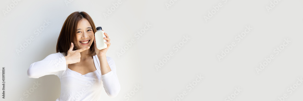 Happy and healthy asian young woman holding and pointing at bottle of fresh and raw wholesome milk, concept of healthy lifestyle with healthy food and drinks Happy and healthy asian young woman holding and pointing at bottle of fresh and raw wholesome milk, concept of healthy lifestyle with healthy food and drinks