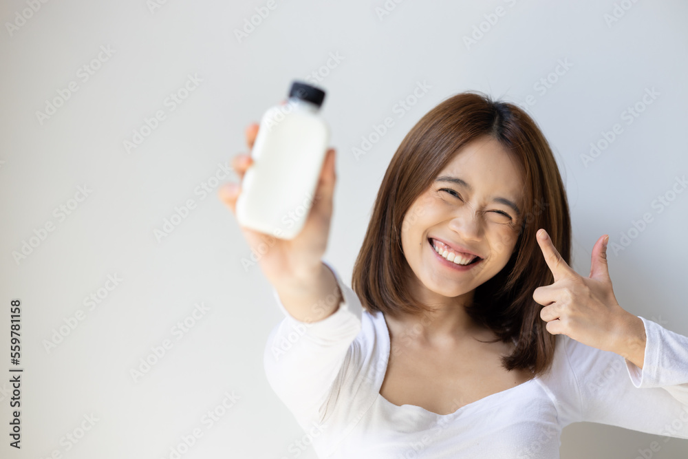Happy and healthy asian young woman holding and pointing at bottle of fresh and raw wholesome milk, concept of healthy lifestyle with healthy food and drinks Happy and healthy asian young woman holding and pointing at bottle of fresh and raw wholesome milk, concept of healthy lifestyle with healthy food and drinks