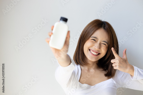Happy and healthy asian young woman holding and pointing at bottle of fresh and raw wholesome milk, concept of healthy lifestyle with healthy food and drinks