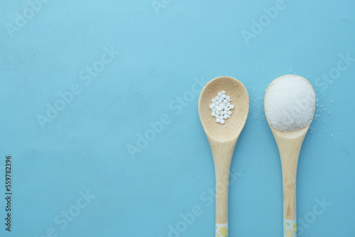 Photos artificial sweetener container comparing with white sugar on wooden spoon